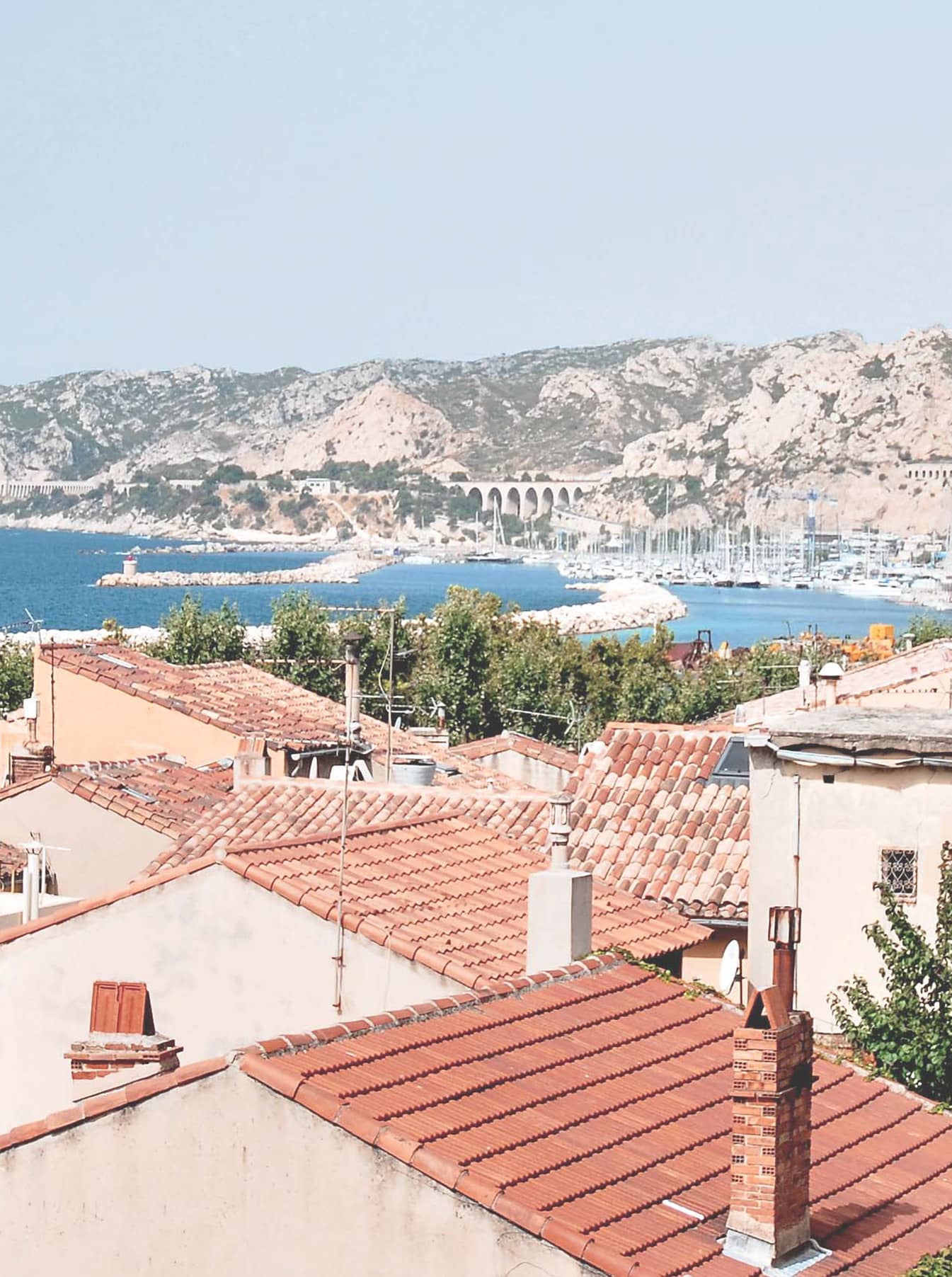 Vue de Marseille avec les toits en tuiles, le port et les reliefs du littoral en arrière-plan.