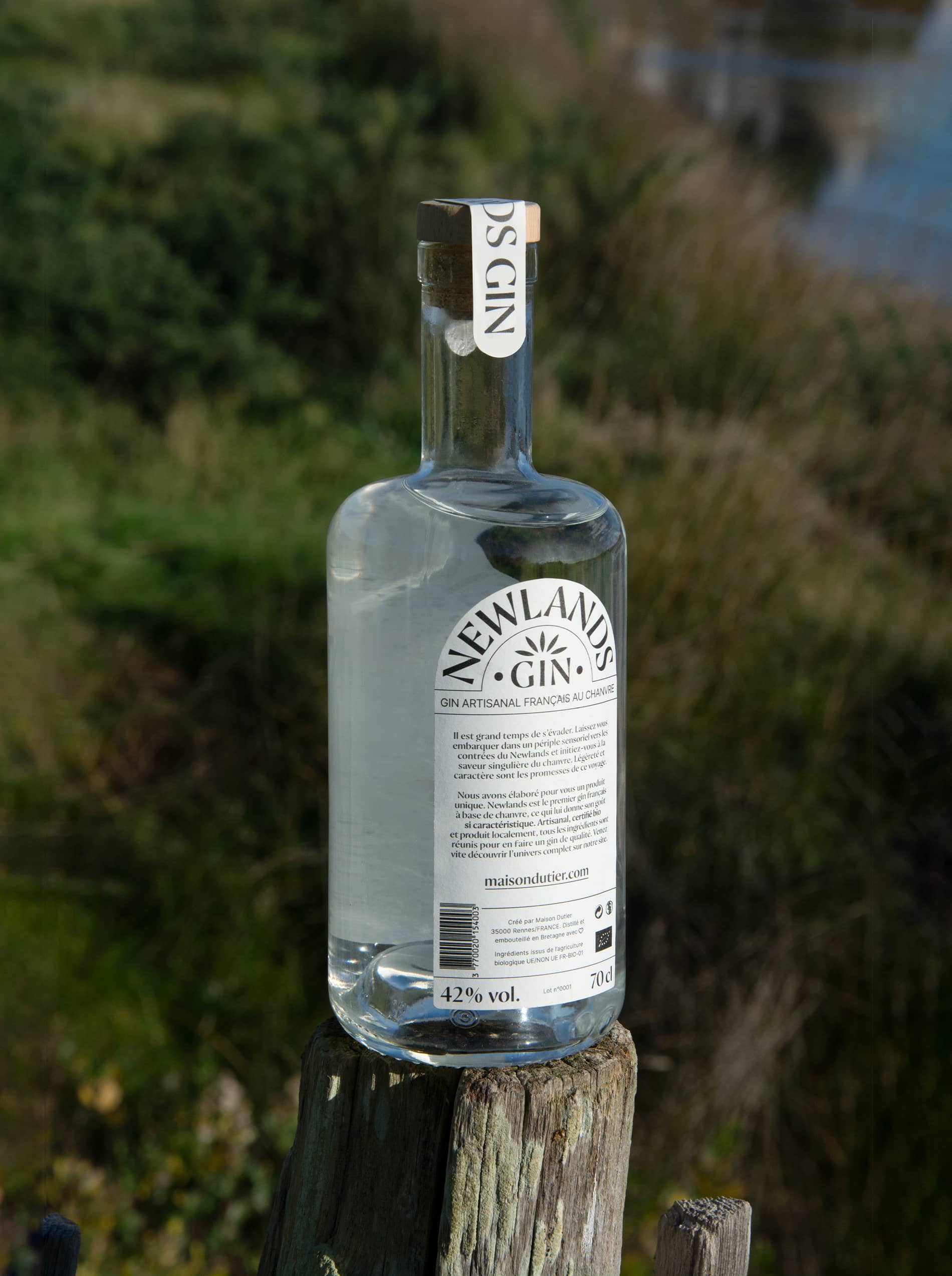 Dos d'une bouteille de gin Newlands sur un poteau en bois avec de la végétation en arrière plan